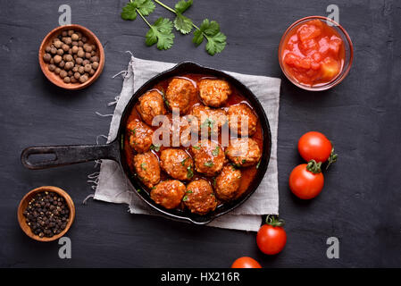 Fleischbällchen mit Tomaten-Sauce und grünen Kräutern in Pfanne auf dunklem Hintergrund, Ansicht von oben Stockfoto