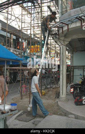 TPerched auf einer Bambus-Leiter arbeiten an Freileitungen oberhalb dieser belebten Straße in Phuket, Thailand Stockfoto