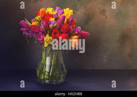 Bouquet von hellen Frühlingsblumen in Vase auf schwarzem Hintergrund, Retro-getönt Stockfoto