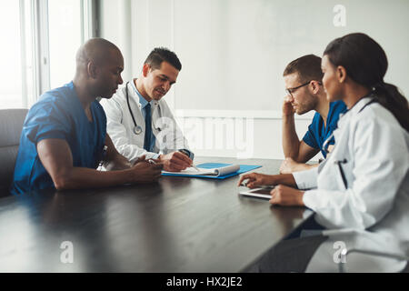 Gemischtrassig Ärzteteam mit einem Treffen mit Ärzten in weißen Kitteln und chirurgische Peelings sitzen an einem Tisch diskutieren eine Patienten-Datensätze Stockfoto