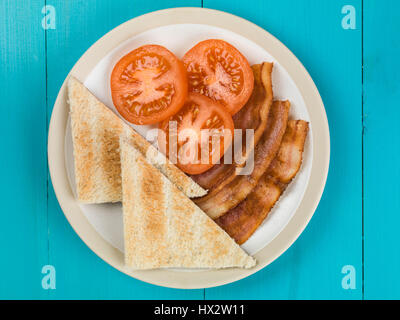 Authentische Flach bunte Englisches Frühstück, gebratenen Speck, Ei, Sunny Side Up, gegrillte Tomaten mit Toast vor einem blauen Hintergrund Stockfoto