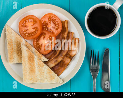 Authentische Flach bunte Englisches Frühstück, gebratenem Speck gegrillte Tomaten mit Toast vor einem blauen Hintergrund und eine Tasse starken Kaffee Stockfoto