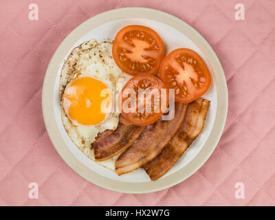 Authentische Flach bunte Englisches Frühstück, gebratenen Speck, Ei, Sunny Side Up, und gegrillten Tomaten gegen einen rosa Hintergrund Stockfoto