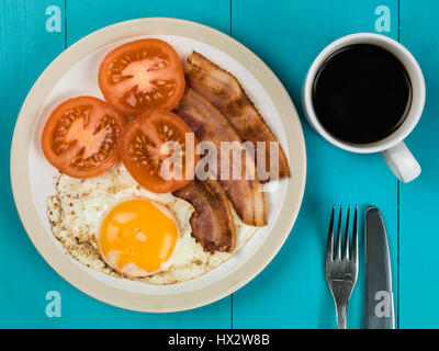 Authentische Flach bunte Englisches Frühstück, gebratenen Speck, Ei, Sunny Side Up, und gegrillten Tomaten vor einem blauen Hintergrund Stockfoto