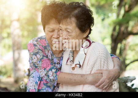 Reportageaufnahme der asiatischen Seniorin tröstet ihre Freundin im Outdoor-Park am Morgen. Stockfoto