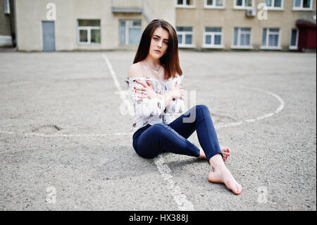 Stilvolle Teenagers Brünette Mädchen auf Hemd, Hose und high Heels Schuhe, sitzen auf Bürgersteig und Hintergrund Schule Hinterhof posierte. Street-Fashion-mod Stockfoto