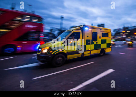 Ein Krankenwagen, der in der Abenddämmerung mit blauen Lichtern in London fährt und an einem roten Bus vorbeifährt Stockfoto