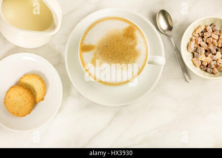 Eine Tasse Latte mit Butter Cookies, ein Glas Milch und Rohrzucker auf einem weißen Marmor Tisch, mit einem Platz für Text. Selektiven Fokus Stockfoto