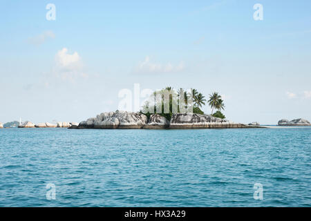 Natürliche Felsen im Meer mit grünen Palmen und Vegetation auf der Insel belitung am Nachmittag und einem weißen Leuchtturm im Hintergrund Stockfoto