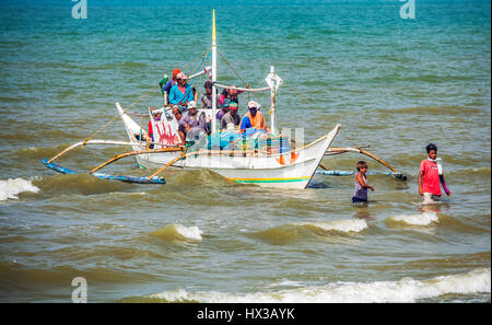 Zwei jungen führen eine überladene Ausleger Angeln Boot Ful Männer und Ufer Baybay Beach, Roxas City, Insel Panay, Philippinen, Südostasien. Stockfoto