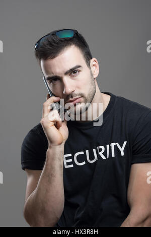 Ernst hart Security-Agent am Telefon Blick in die Kamera sprechen. Atmosphärische kontrastreich Porträt über graue Studio-Hintergrund. Stockfoto