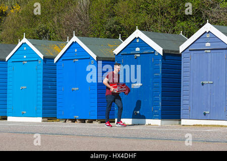 Bournemouth, Dorset, UK. 25. März 2017. UK-Wetter: schönen warmen, sonnigen Tag als Besucher gehen ans Meer machen das Beste aus der Sonne an den Stränden von Bournemouth. Junger Mann tragenden Kasten Budweiser Bier Promenade vorbei an blauer Strandhütten am Strand von Bournemouth. Bildnachweis: Carolyn Jenkins/Alamy Live-Nachrichten Stockfoto