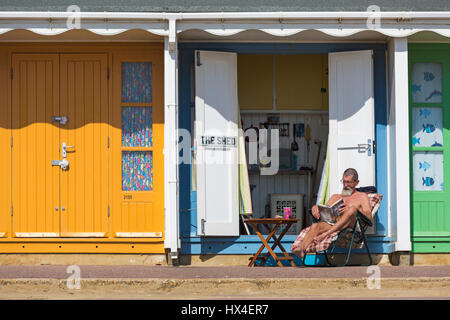 Bournemouth, Dorset, UK. 25. März 2017. UK-Wetter: schönen warmen, sonnigen Tag als Besucher gehen ans Meer machen das Beste aus der Sonne an den Stränden von Bournemouth. Mann sitzt im Stuhl Liege am Strand Hütte zum Sonnenbaden entspannen und David Baldacci Buch The Escape Stockfoto