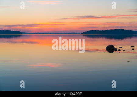 DIE SCHWEDISCHEN SCHÄREN IN DER OSTSEE BEI SONNENAUF- ODER SONNENUNTERGANG MIT REICHEN FARBEN UND FELSEN IM VORDERGRUND MIT REFLEXIONEN Stockfoto