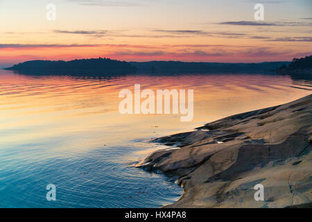 DIE SCHWEDISCHEN SCHÄREN IN DER OSTSEE BEI SONNENAUF- ODER SONNENUNTERGANG MIT REICHEN FARBEN UND FELSEN IM VORDERGRUND MIT REFLEXIONEN Stockfoto