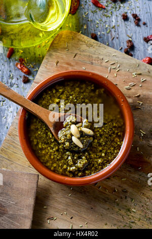 High-Angle Shot eine Steingut-Schale mit Italienische Pesto-Sauce garniert mit einigen Pinienkernen auf ein Schneidebrett neben einer Menage mit Olivenöl auf eine r Stockfoto