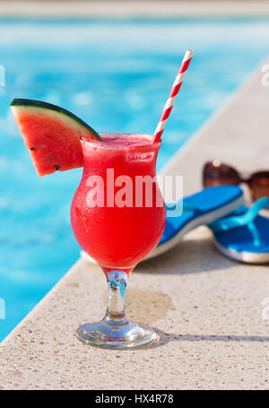 Wasser Melone rot frisch Orangensaft Smoothie Drink cocktail Hausschuhe und eine Sonnenbrille in der Nähe von Schwimmbad Stockfoto