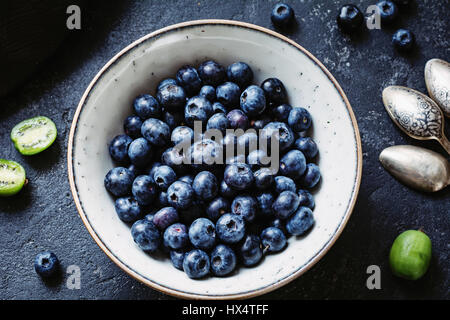 Draufsicht der frische Heidelbeeren in weiße Keramikschale auf dunklen Steintisch. Closeup Stockfoto