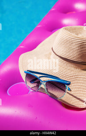 Sonnenbrillen und Strohhut auf einem rosa Luftmatratze im Pool. Tropischer Sommer Konzept. Stockfoto