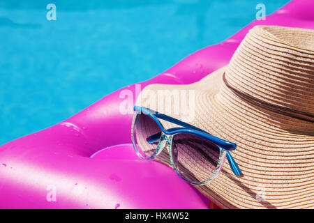 Sonnenbrillen und Strohhut auf einem rosa Luftmatratze im Pool. Tropischer Sommer Konzept. Stockfoto