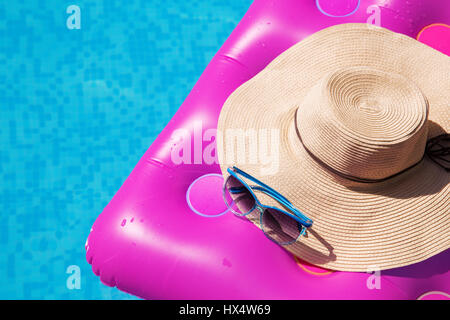 Sonnenbrillen und Strohhut auf einem rosa Luftmatratze im Pool. Tropischer Sommer Konzept. Stockfoto