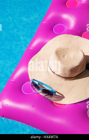 Sonnenbrillen und Strohhut auf einem rosa Luftmatratze im Pool. Tropischer Sommer Konzept. Stockfoto