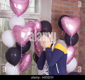 Traurig oder glücklich Mann bedeckte sein Gesicht. Bunte Luftballons auf Hintergrund. Stockfoto