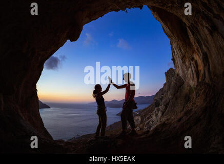 Paar Kletterer geben hohe fünf und jubeln, in Höhle bei Sonnenuntergang Stockfoto