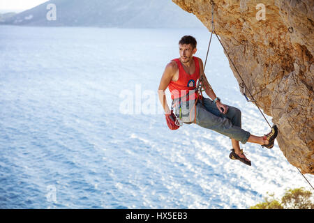 Männliche Kletterer ruhen, während die hängen am Seil vor dem nächsten Versuch auf anspruchsvolle route Stockfoto