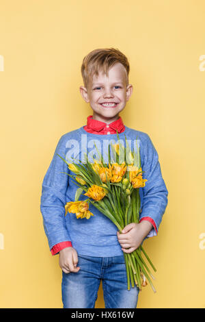 Kleines schönes Kind mit einem Strauß Tulpen. Sohn macht Mutter Blumen zum Frauentag, Muttertag. Geburtstag. Zum Valentinstag. Frühling. Stockfoto