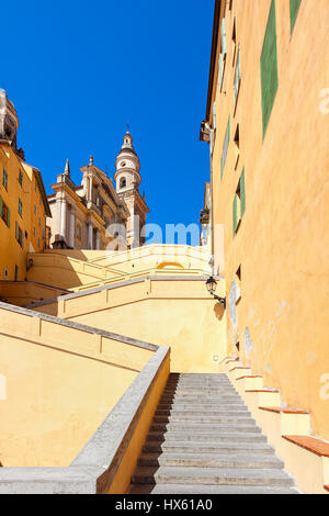 Treppen unter bunten Wände in Richtung Basilika Saint-Michel Archange unter blauem Himmel in Menton, Frankreich ("vertikale Zusammensetzung"). Stockfoto