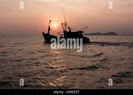 Eine alte hölzerne Angeln Boot Köpfe heraus zum Meer bei Sonnenuntergang hinter sich. Stockfoto