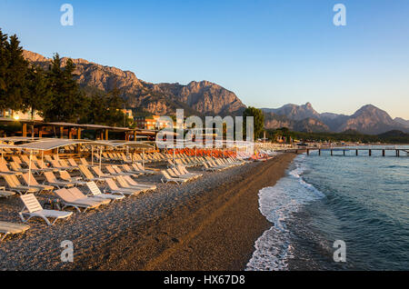 Hotel und Plank Betten mit Sonnenschirmen am Strand vor dem Hintergrund der Berge. Kemer.Turkey. Sonnenaufgang im Meer. Stockfoto