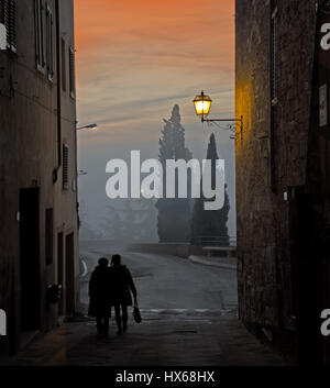 Zwei Damen gehen auf eine S. Quirico wenig Straße, ein schönes kleines Dorf in der Nähe von Siena, Italien in einem nebligen Wintertag in der Abenddämmerung Stockfoto