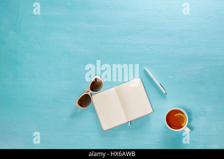 Flache Laien Zusammensetzung Tagebuch, Brille, Stift und Tasse Tee auf blauen hölzernen Schreibtisch. Stockfoto