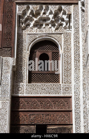 Meknès, Marokko.  Medersa Bou Inania, 14.. Jahrhundert.  Florale Dessins in Stuck und Holz und Kalligraphie, um ein Fenster aus dem Innenhof zu sehen. Stockfoto