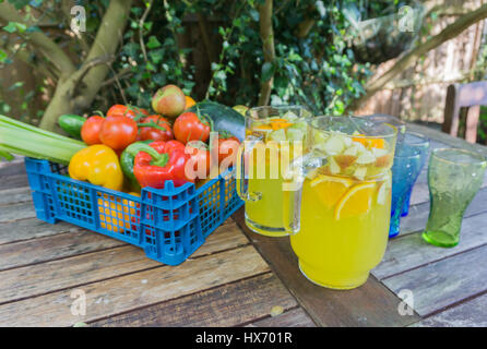 Anzeige von Obst und Gemüse mit einem Krug Orangensaft und Gläser auf einem Tisch draußen in einem Garten Stockfoto