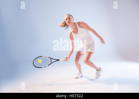 Attraktive junge Tennisspielerin mit Schläger schlagen Ball auf blau Stockfoto