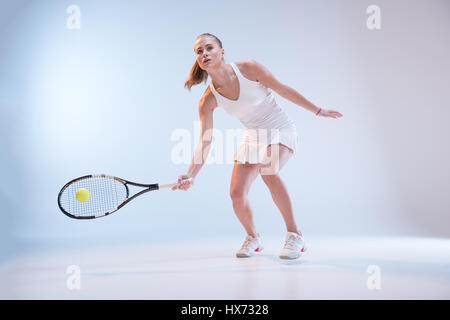 Aktive junge Tennisspielerin in Sportbekleidung Kollision Ball mit Schläger Stockfoto