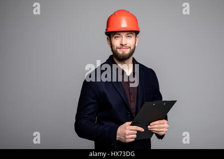 Mann in einem schwarzen Anzug und Bau Helm Blick zur Seite und halten schwarz auf grau Stockfoto