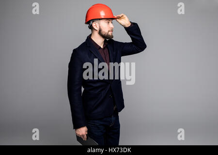 Mann in einem schwarzen Anzug und Bau Helm Blick zur Seite und halten schwarze Ordner auf grauem Hintergrund Stockfoto