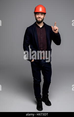 Mann in einem schwarzen Anzug und Bau Helm Blick zur Seite und halten schwarze Ordner auf grauem Hintergrund Stockfoto