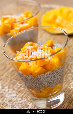Gesundes Frühstück. Chia Pudding mit Mango im Glas Gläser, halbe Mango auf Stroh Hintergrund. Selektiven Fokus Stockfoto