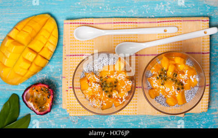 Gesundes Frühstück. Chia Pudding mit Mango im Glas Gläser, Mango Hälften, Passionsfrucht/Maracuja auf einem blauen Hintergrund aus Holz. (Ansicht von oben) Stockfoto