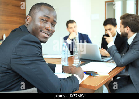 Lächelt zuversichtlich afrikanischen Geschäftsmann in einem Gespräch mit einer Gruppe von Rassen Mitarbeiter am Konferenztisch im Büro sitzen Stockfoto