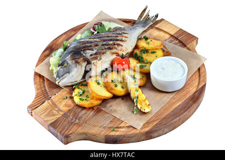 Gegrillter Fisch Dorado auf einem runden Holzbrett mit einem Blatt Pergament, Gemüse und Sauce, isoliert auf weißem Hintergrund. Stockfoto