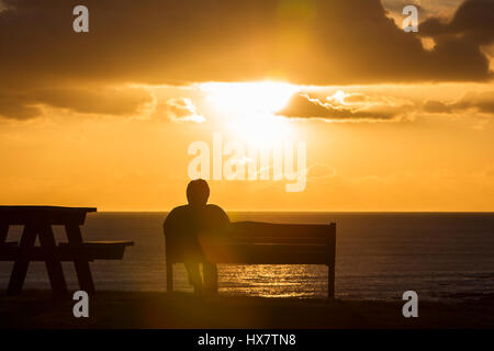 Eine Frau nimmt in den dramatischen Sonnenuntergang aus Armband Bucht, Mumbles, UK Stockfoto