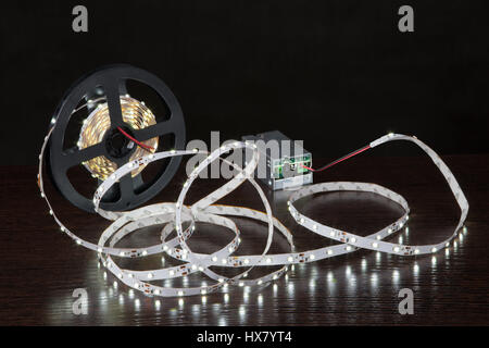 Leuchtende LED-Lichtleiste auf der Spule, in der Nähe von der Stromversorgung, auf einem schwarzen Hintergrund. Stockfoto