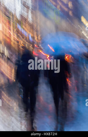 Zusammenfassung Hintergrund Menschen eilen nach unten die Stadtstraße in regnerischen Abend, Schaufenster. Vorsätzliche Bewegungsunschärfe. Konzept der Jahreszeiten, Wetter, moderne Stadt. Stockfoto