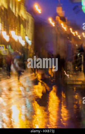 Zusammenfassung Hintergrund unscharf Personen unter Sonnenschirmen, Stadtstraße in regnerischen Abend, Orange-braune Töne vorsätzliche Bewegungsunschärfe. Konzept der Jahreszeiten, Wetter, moderne Stadt. Stockfoto
